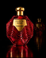 Red textured glass Fleur Noir perfume bottle with a gold cap and gold label against a black background.